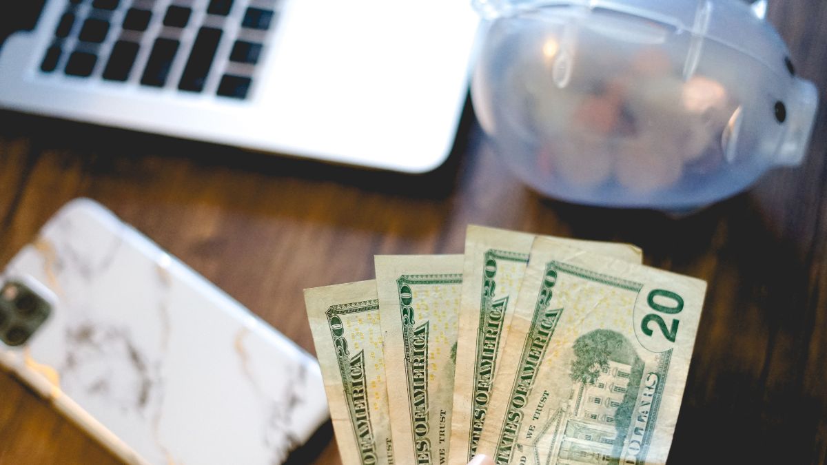 Dólares sobre uma mesa com smartphone simbolizando o estímulo para a abertura de conta em dólar no Brasil