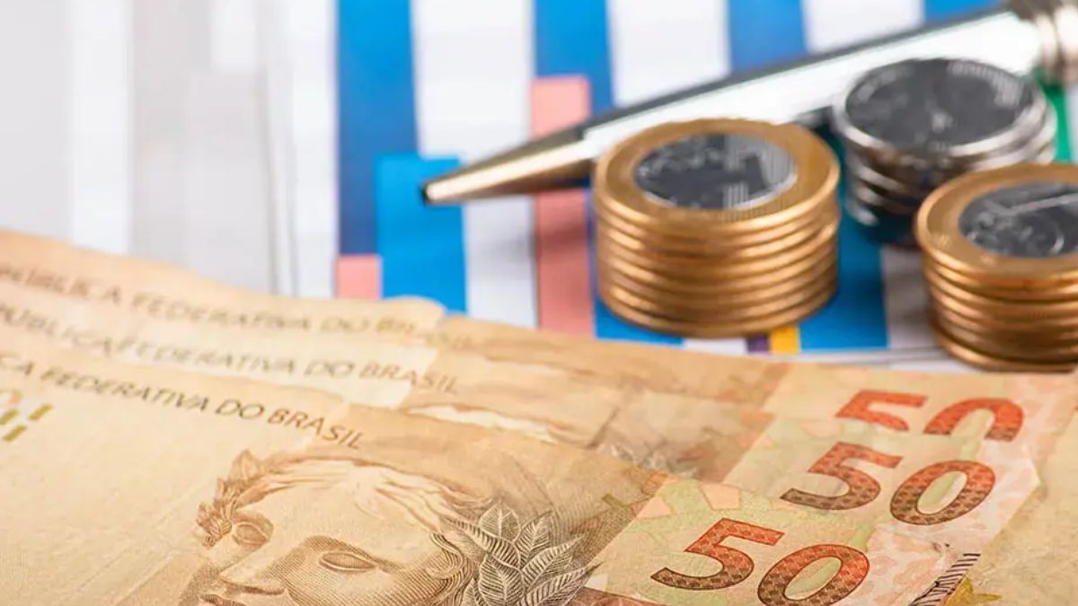 Cédulas e moedas de Real junto a uma caneta, simbolizando a explosão de novos contratos de crédito consignado privado