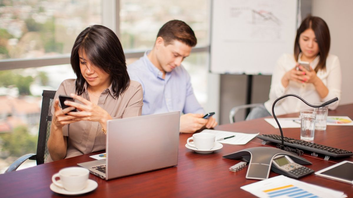 Colaboradores olhando o celular no escritório para ilustrar o risco de perda de produtividade nas empresas