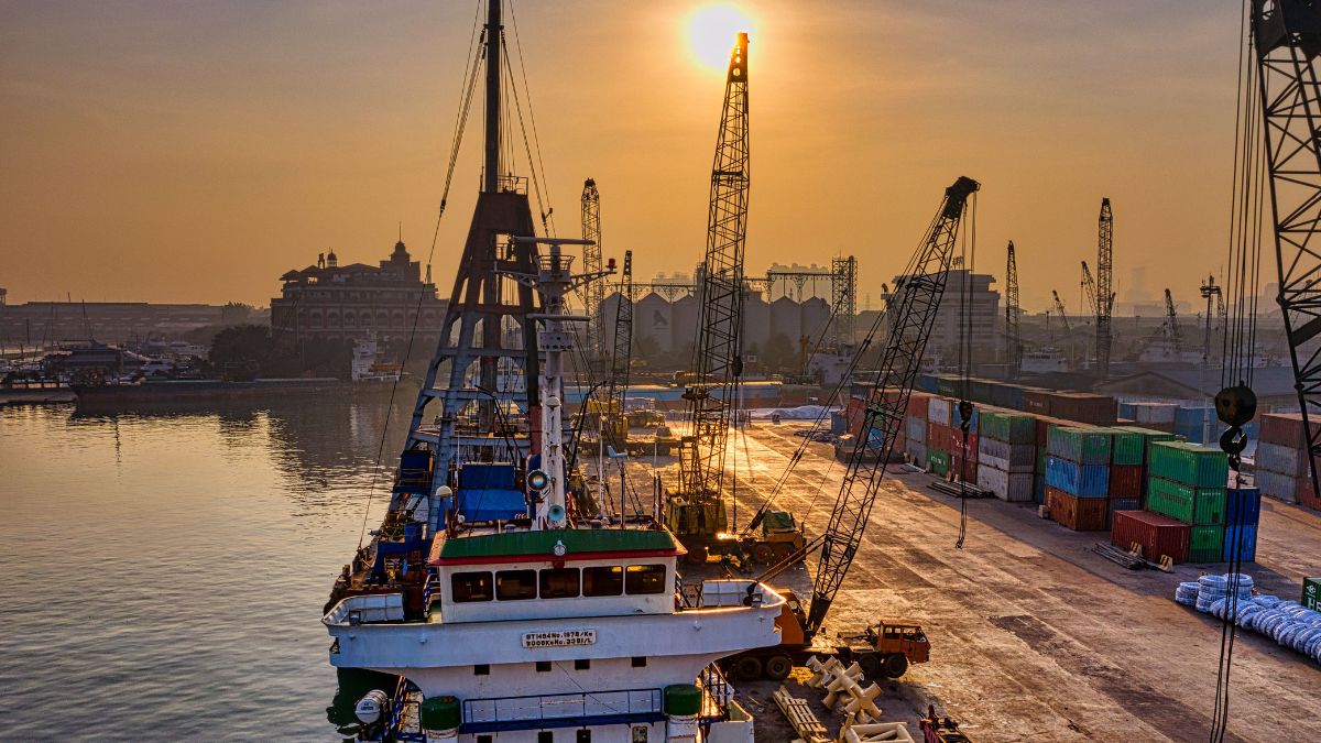 Navio cargueiro atracado em terminal portuário com guindastes durante o pôr do sol, ilustrando a logística que influencia o preço dos fertilizantes no Brasil.