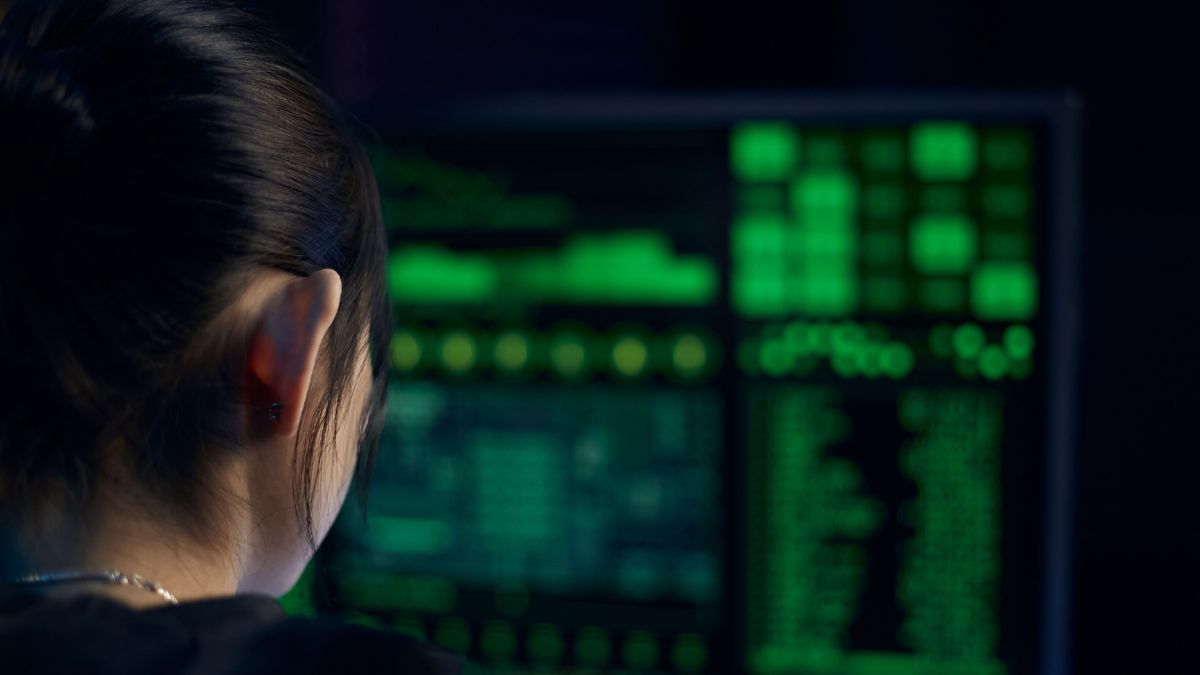 Analista de cibersegurança observa monitor com códigos e dados digitais em sala escura, ilustrando a investigação sobre o vazamento de senha da Defesa Civil.