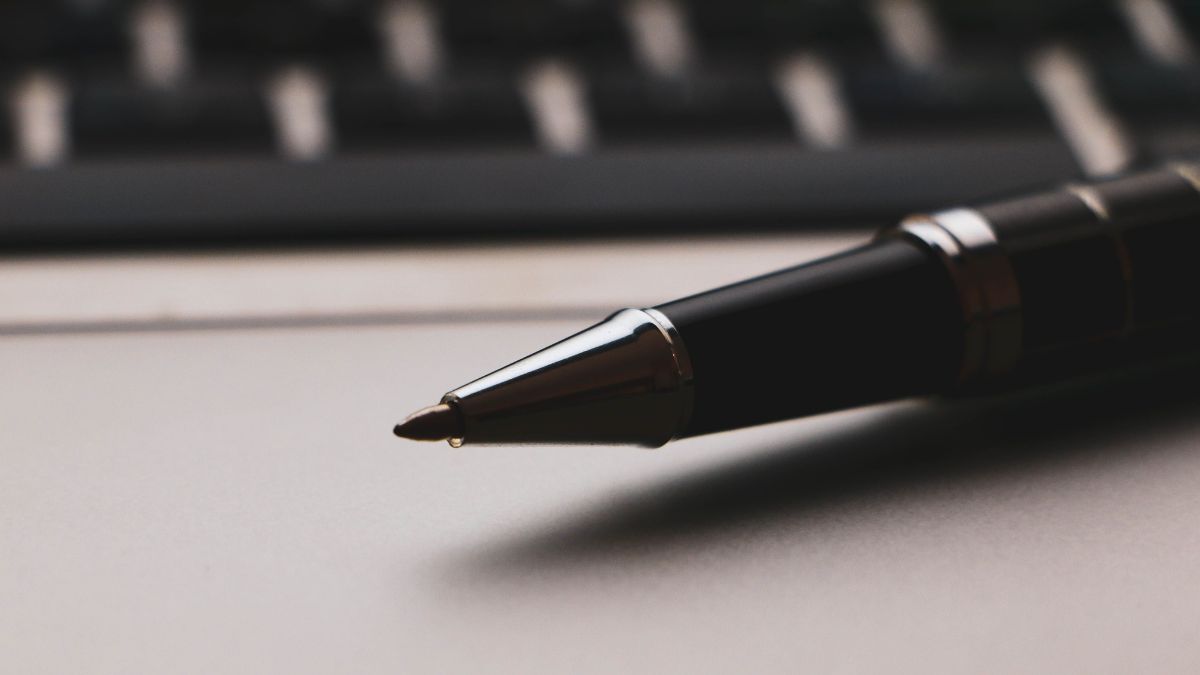 Caneta perto do teclado do computardor, sugerindo uma assinatura ou decisão que virá da próxima reunião do Banco Central, a partir do resultado do IPCA abaixo da expectativa em junho