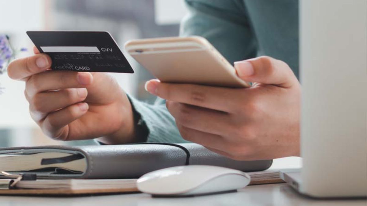 Mão segurando smartphone e cartão de crédito para simbolizar que o Banco Central busca conter o endividamento das famílias